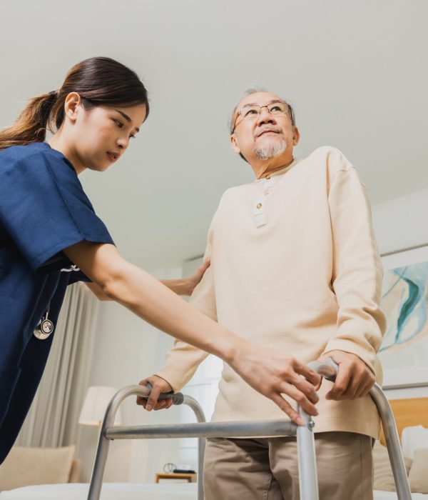 Smiling nurse woman helping senior Asian man to walk around the nursing home, use walker with strong health and Help and care concept