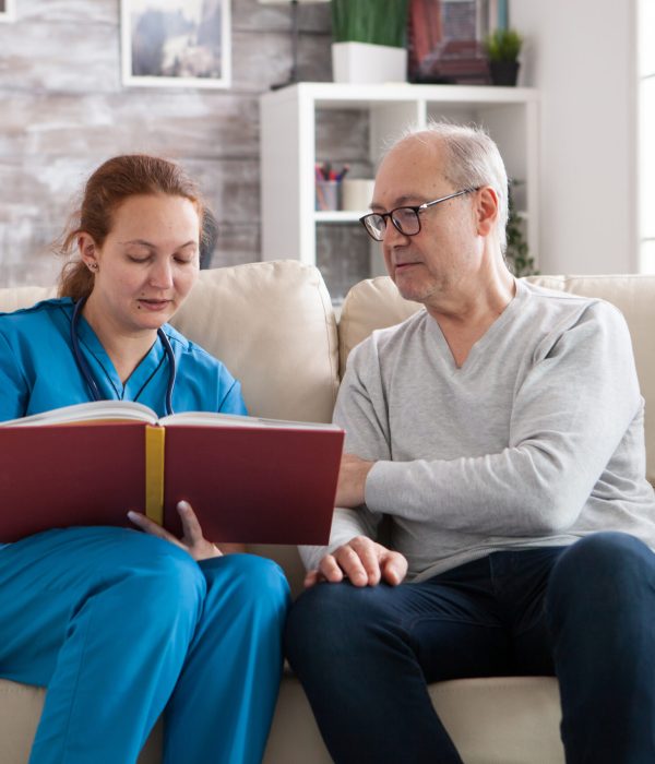 Young female doctor reading a book for old man in nursing home.